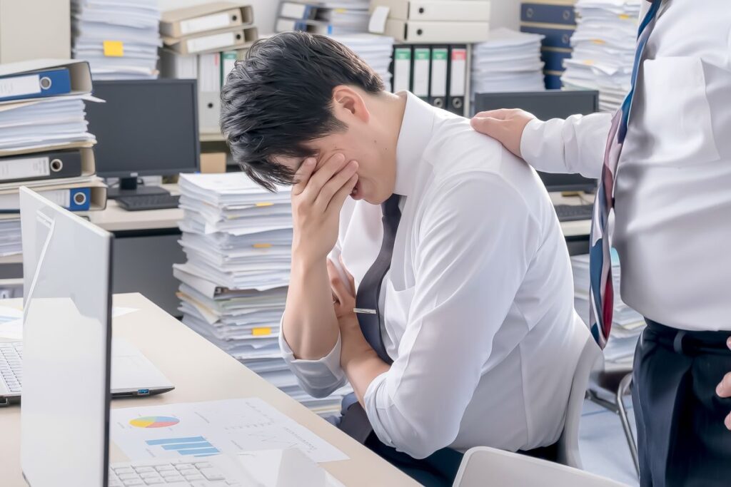 書類の山を前に頭を抱える会社員