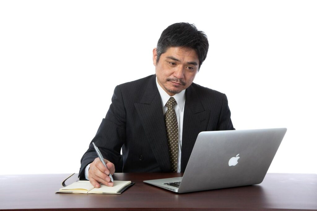 ノートパソコンを見ながらメモを取るビジネスパーソン