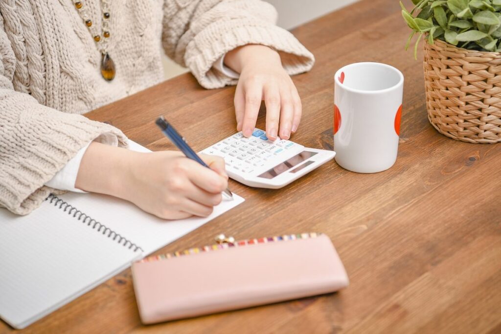 ノートに書き込みながら電卓で計算する手元
