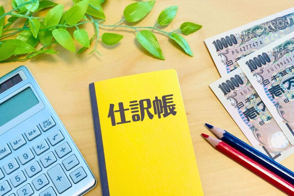 「仕訳帳」と書かれたノートと電卓
